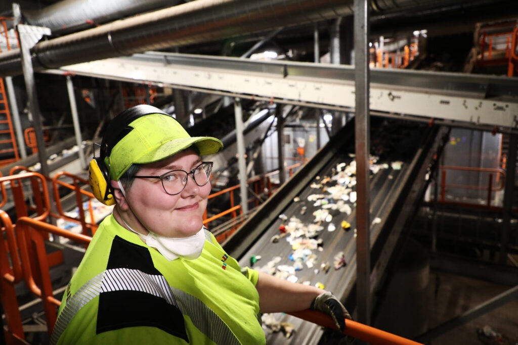 Kvinna i arbetskläder står i lokal för plaståtervinning.