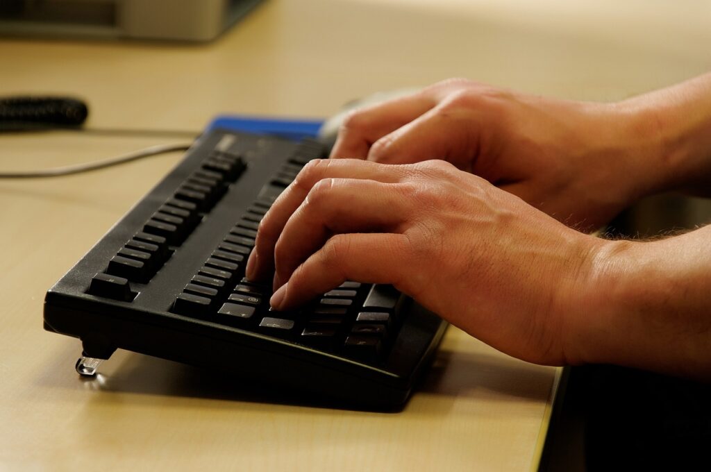 Någon skriver vid datorn. Bilden visar bara händerna och ett svart tangetbord.