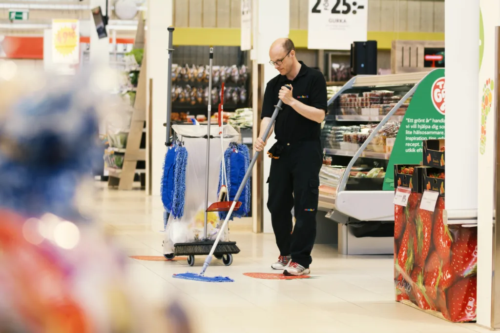 En man i Samhallkläder står och städar inne i en livsmedelbutik.