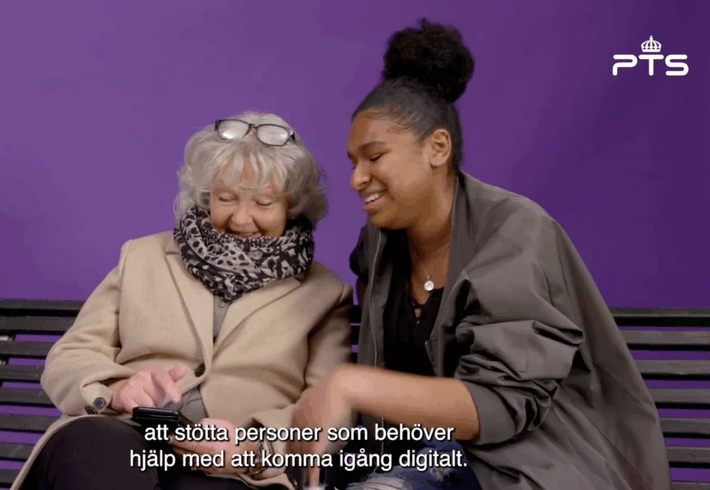 Två kvinnor som hjälps åt med att göra något med en mobiltelefon.