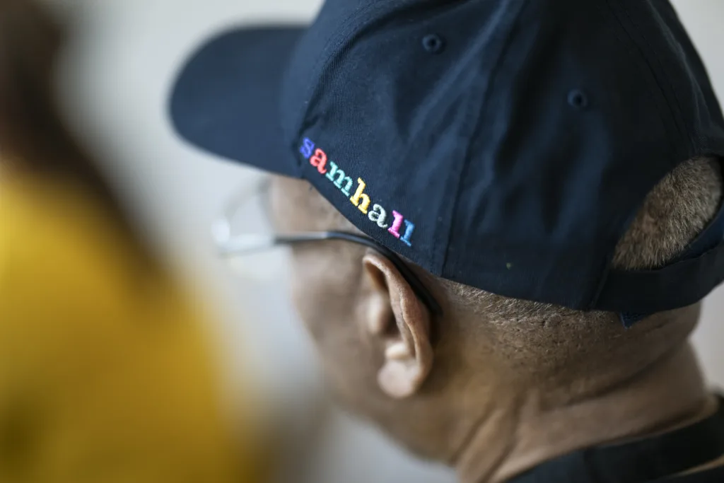 En man i glasögon och marinblå keps. På kepsens vänstra sida finns Samhalls logga. Mannen vänder sig bort från kameran.