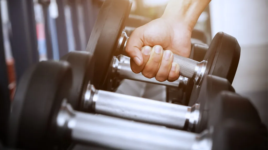 En person greppar en hantel ur ett hantelställ.